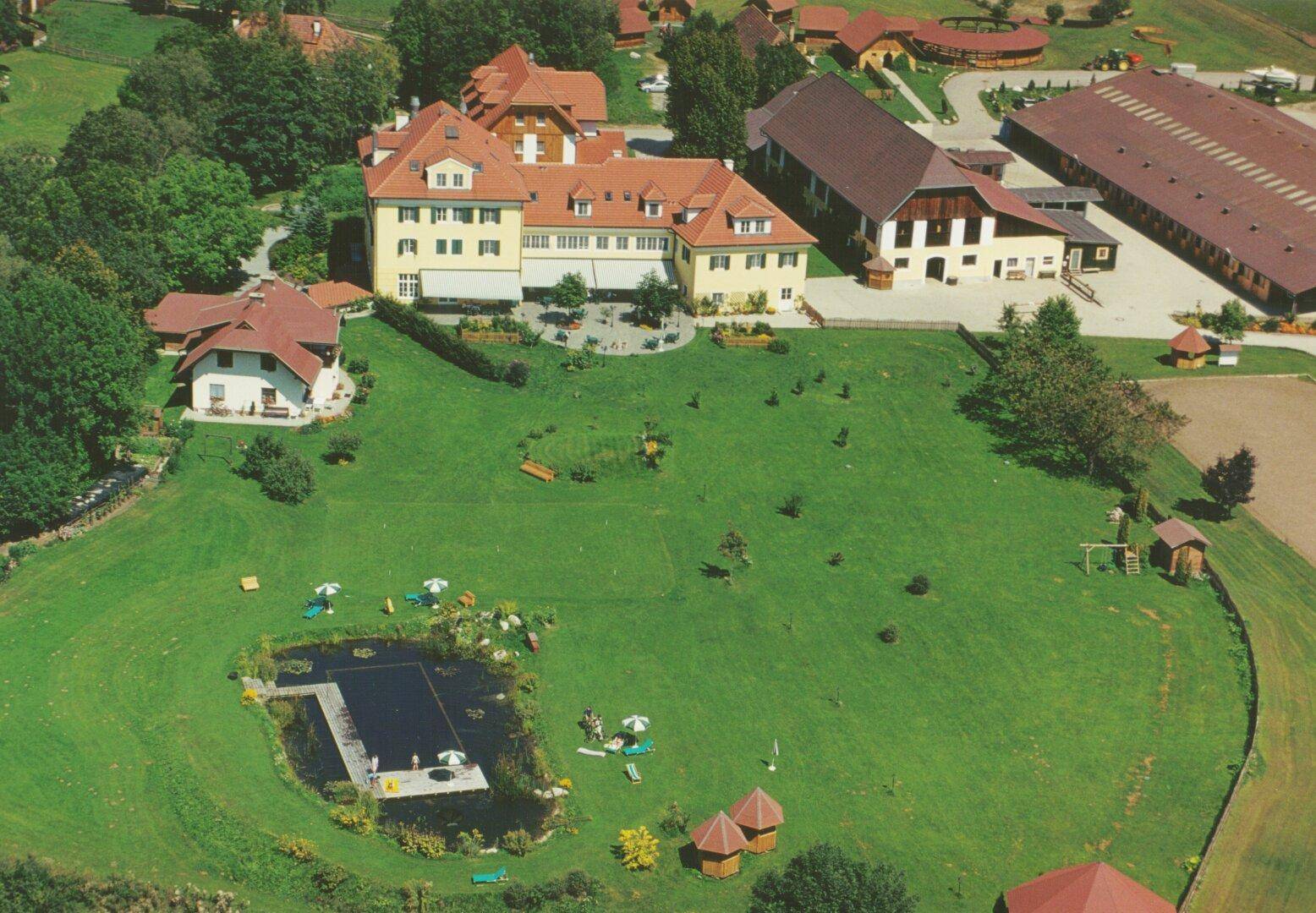 Luftaufnahme eines Anwesens mit großem Garten, Teich und mehreren Gebäuden in ländlicher Umgebung.
