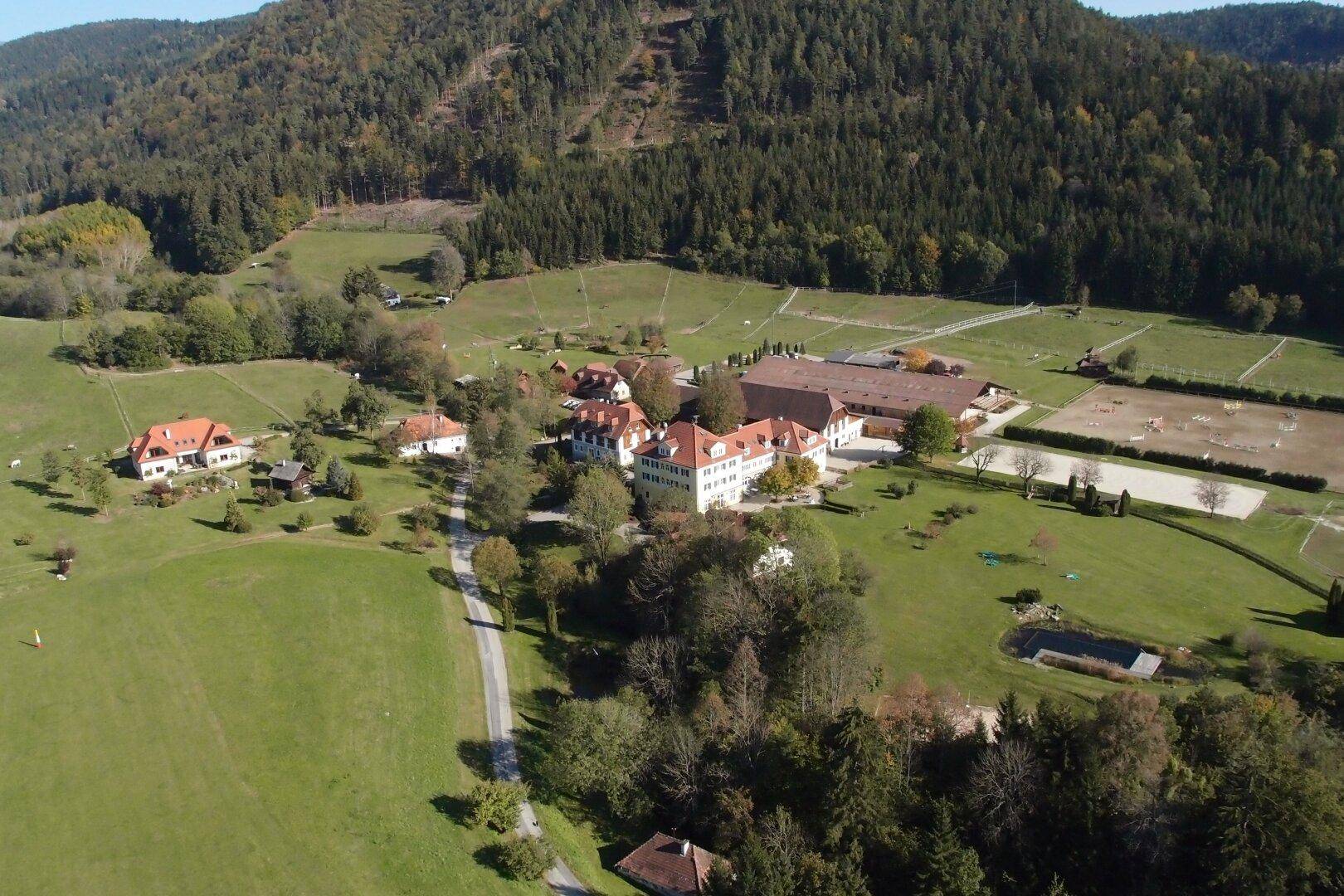 Luftaufnahme eines weitläufigen Anwesens mit mehreren Gebäuden, Wegen und grünen Flächen in ländlicher Lage.