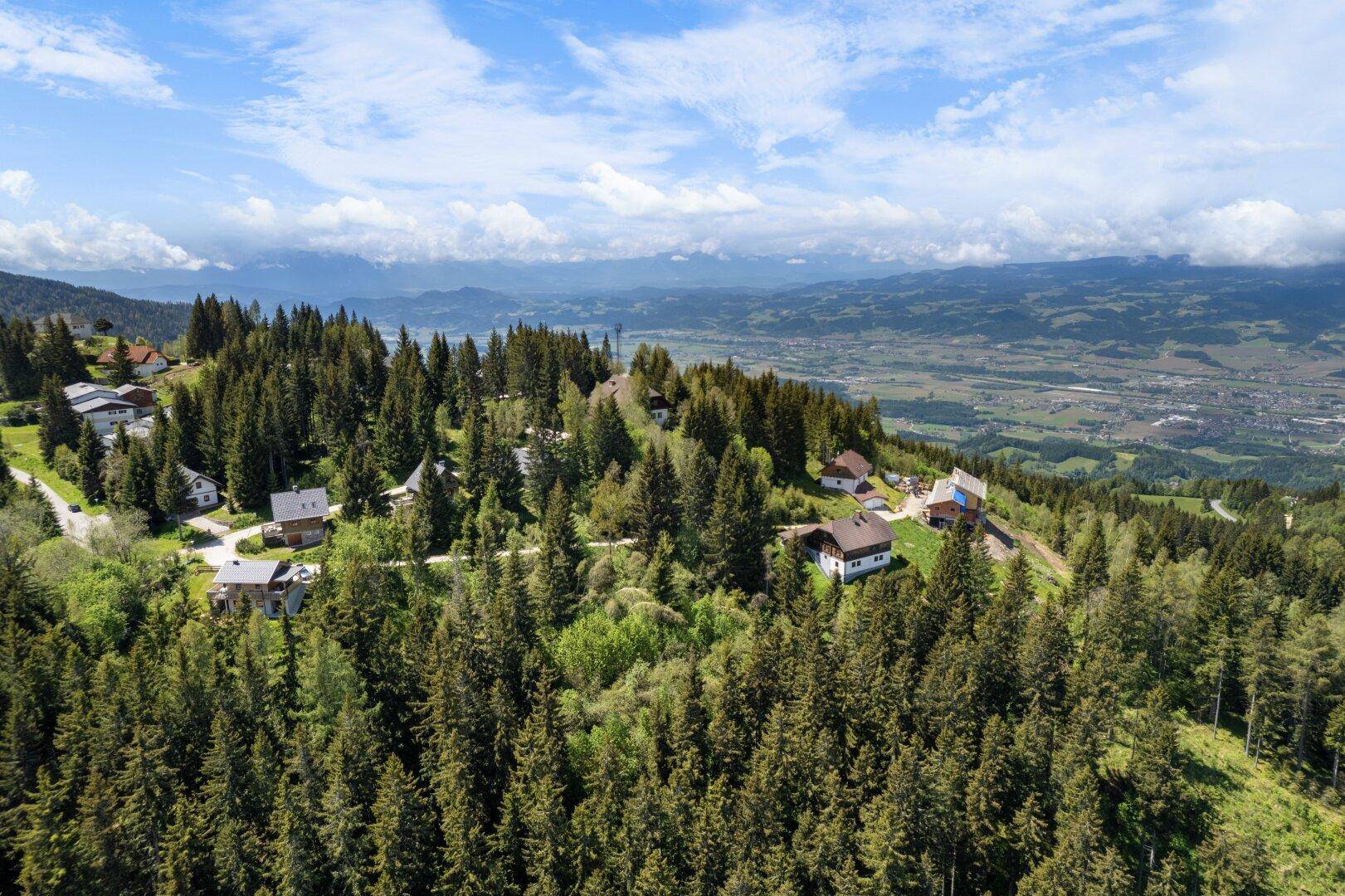 Panoramablick über eine bewaldete Bergregion mit verstreuten Häusern und weitem Talblick.