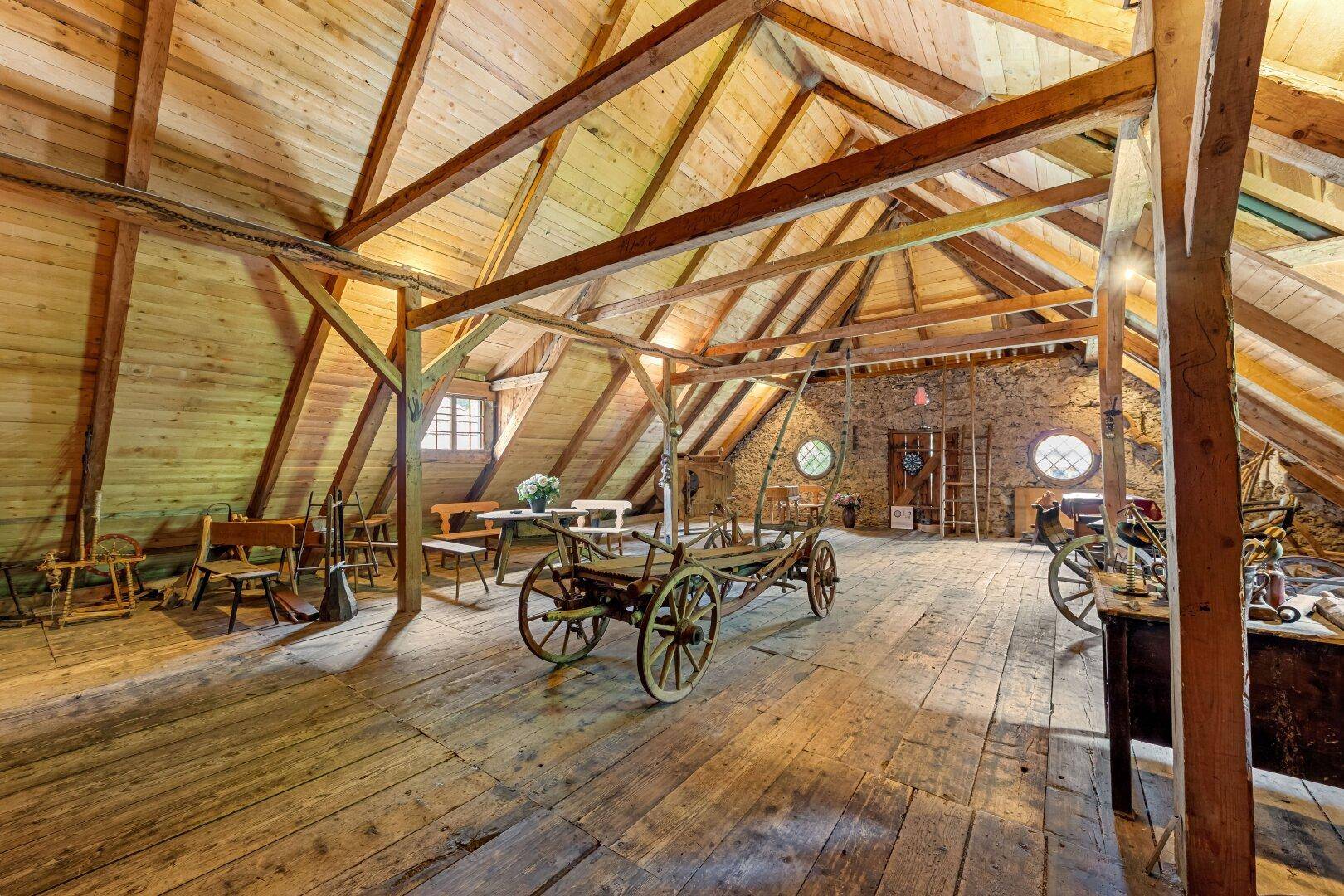 Geräumiger Dachboden mit sichtbarer Holzkonstruktion, Holzboden und historischen Wagen.