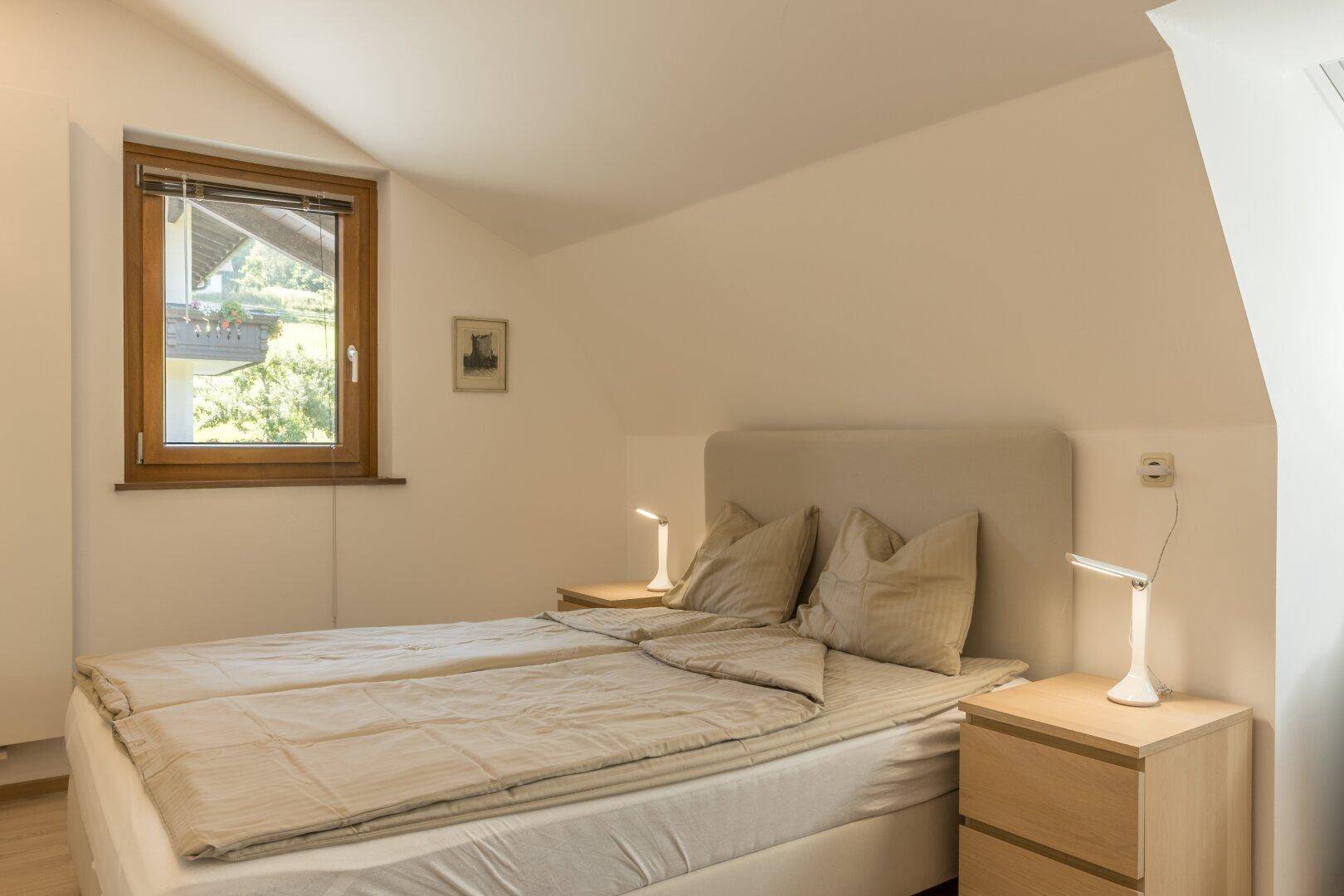 Gemütliches Schlafzimmer mit Doppelbett, Nachttischen und Dachschräge, bietet eine ruhige Atmosphäre.