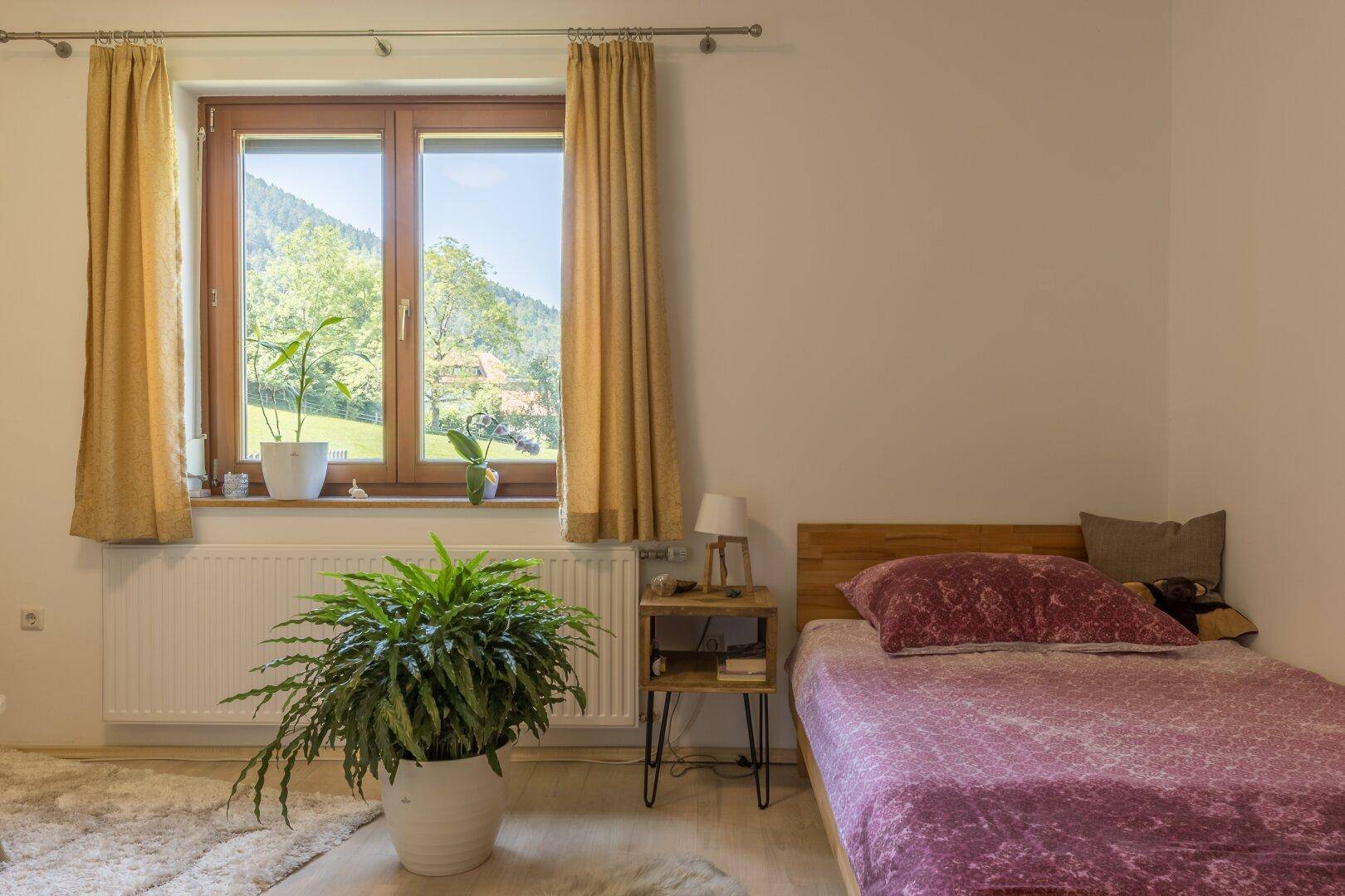 Helles Schlafzimmer mit Einzelbett, großem Fenster und Blick ins Grüne, sehr einladend.