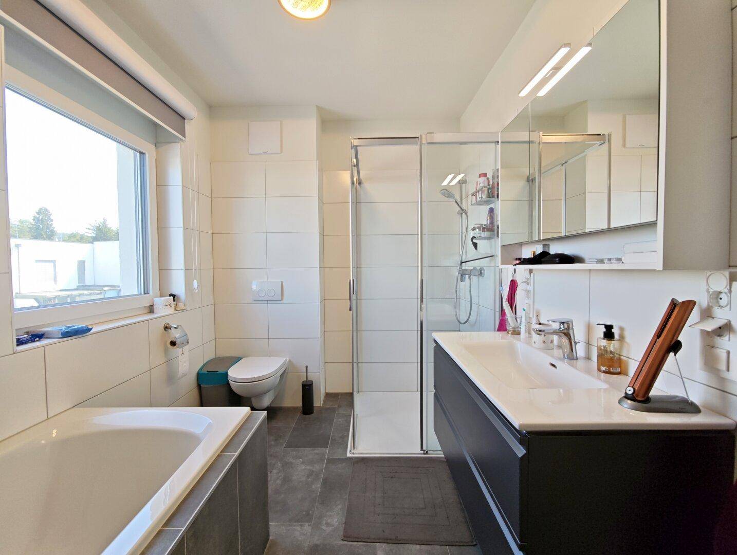 Modernes Badezimmer mit Badewanne, Duschkabine, Einzelwaschbecken und Fenster.