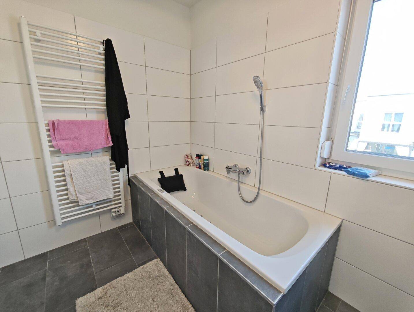 Badewanne mit Handbrause und beheiztem Handtuchhalter in hellem Badezimmer.