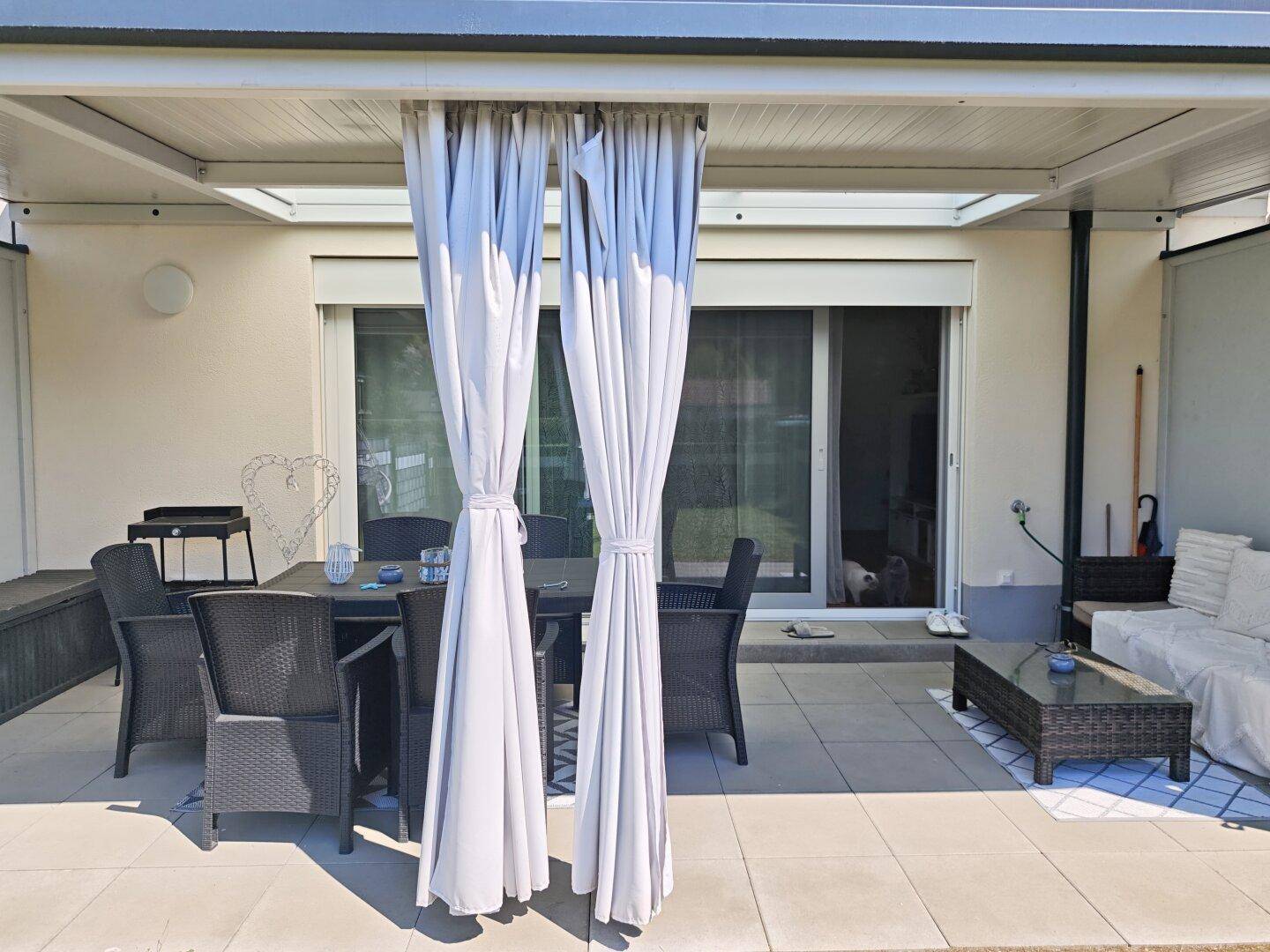 Geräumige überdachte Terrasse mit Vorhängen und Zugang zum Wohnbereich.
