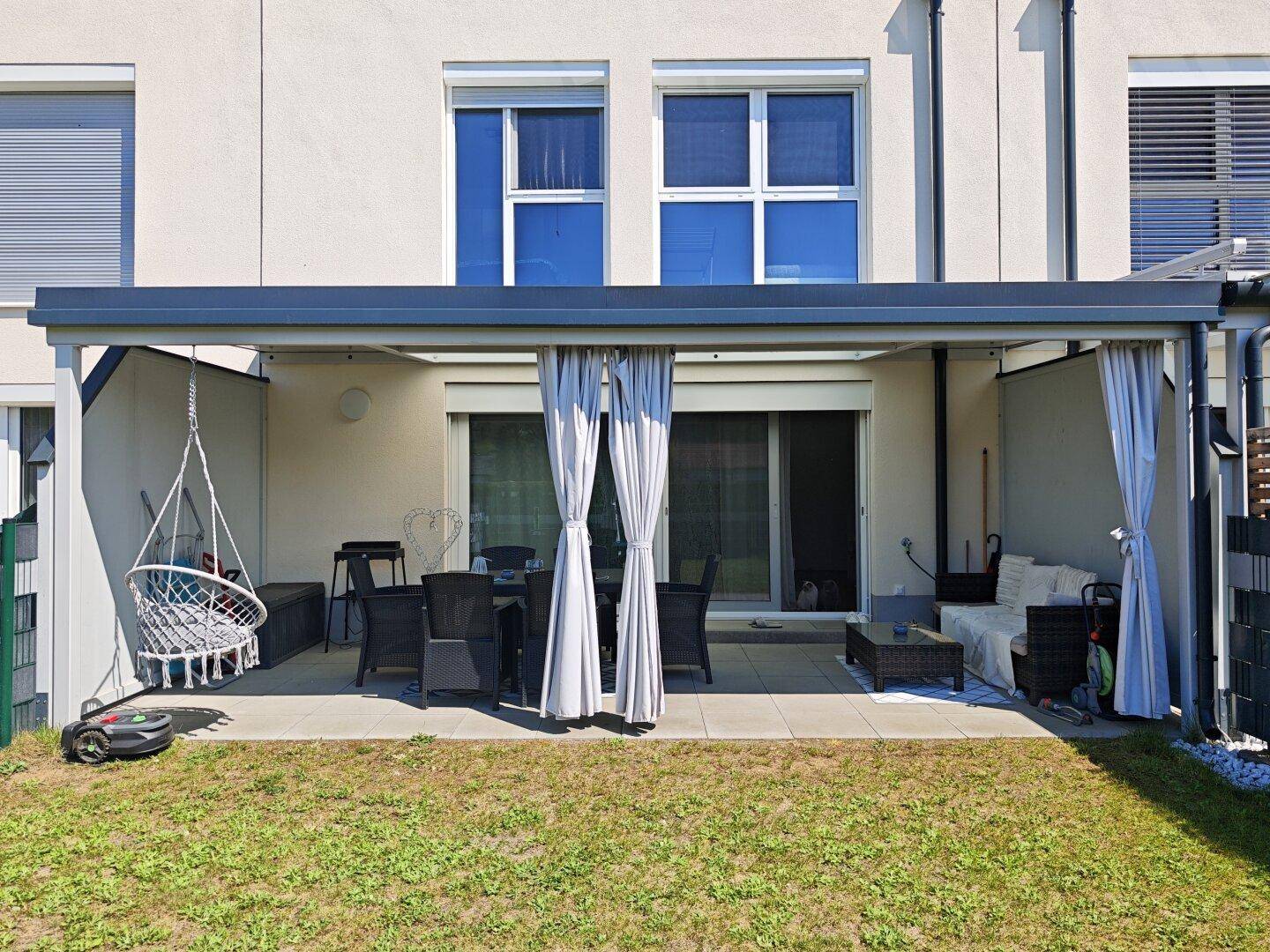 Überdachte Terrasse mit Hängesessel und Blick auf den Gartenbereich.