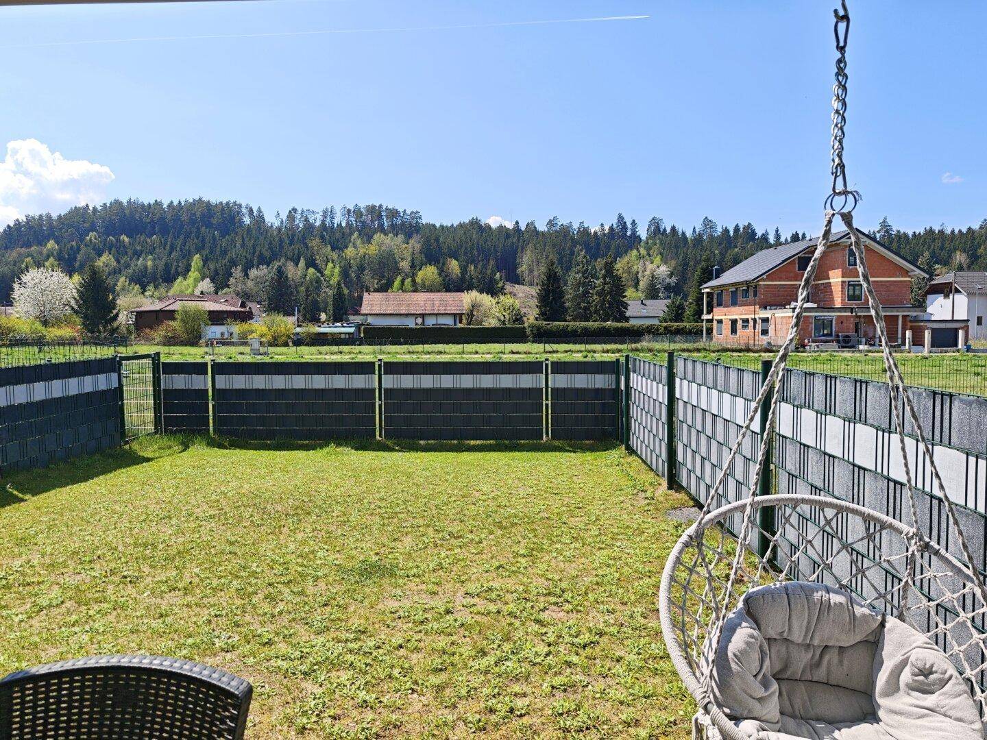 Gepflegter Gartenbereich mit Rasenfläche und Hängesessel, umgeben von Natur.