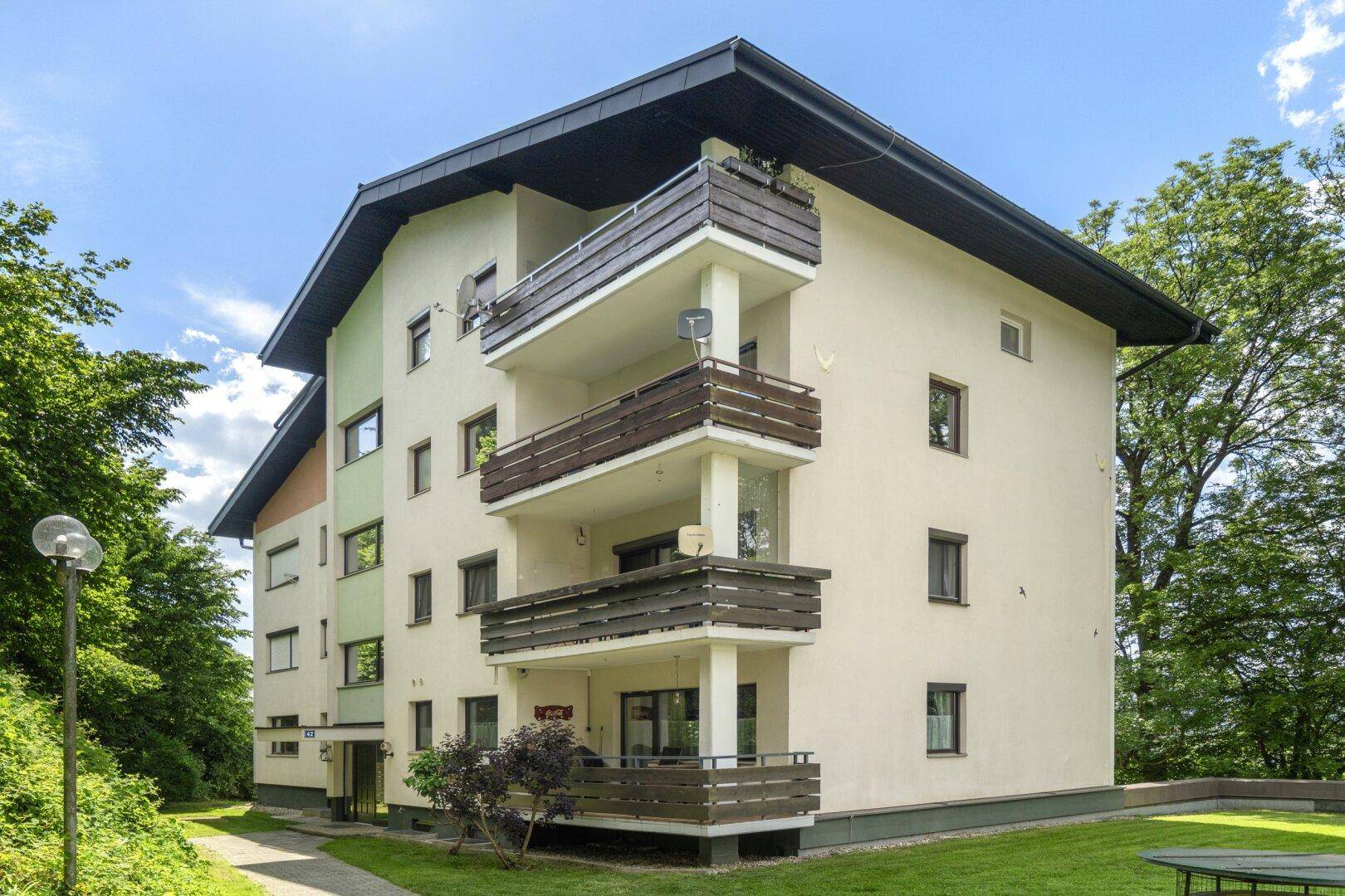 Seitenansicht des Mehrfamilienhauses mit mehreren Balkonen und gepflegter Grünfläche.