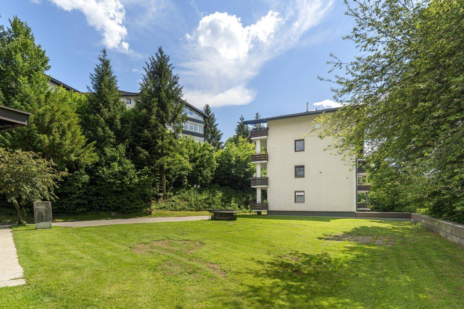 Große, gepflegte Rasenfläche neben dem Gebäude, umgeben von Bäumen und Sträuchern.