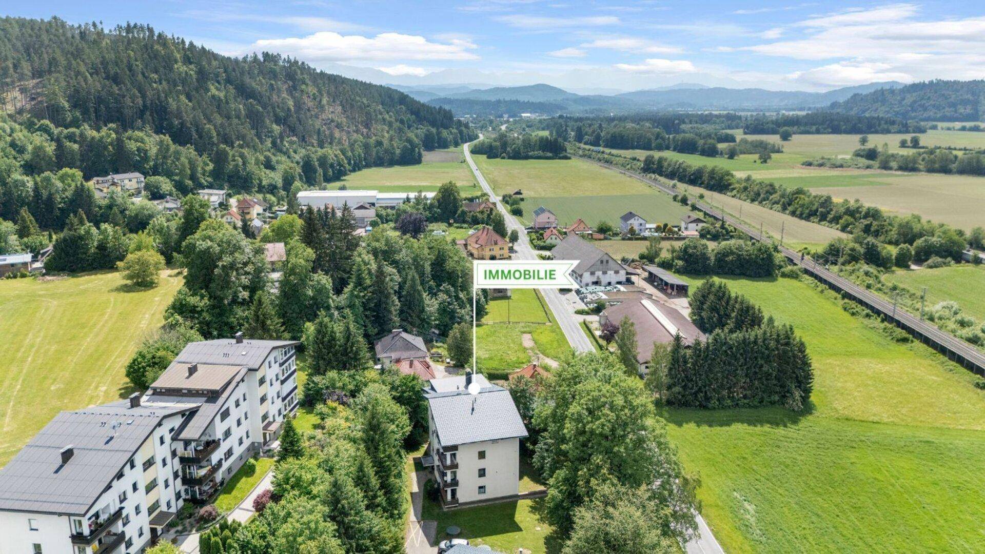 Luftaufnahme der Immobilie in einer grünen Umgebung mit Bergen im Hintergrund und umliegenden Feldern.