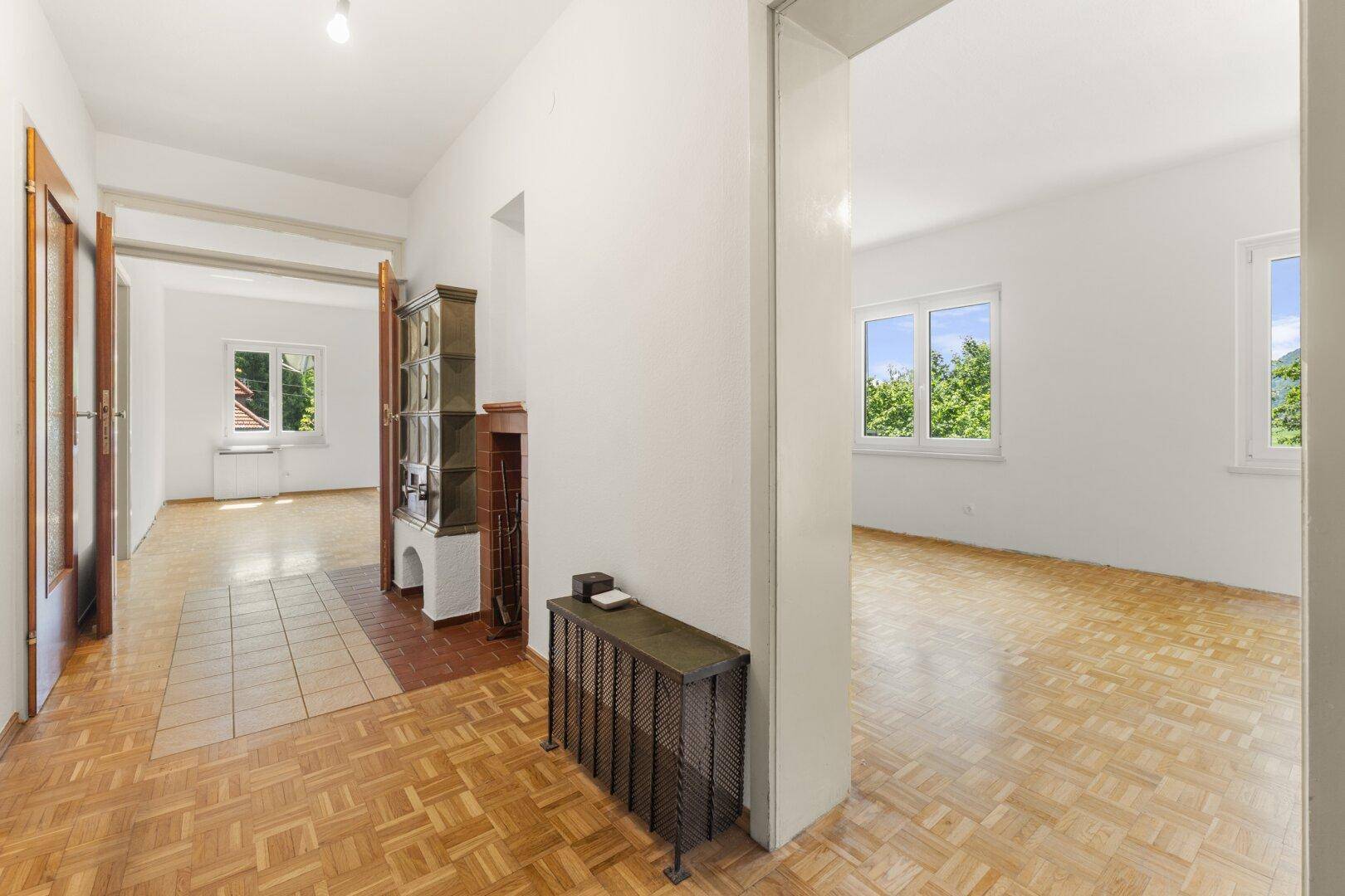 Heller Flur mit Parkettboden und Zugang zu weiteren Zimmern, inklusive eines Kachelofens.