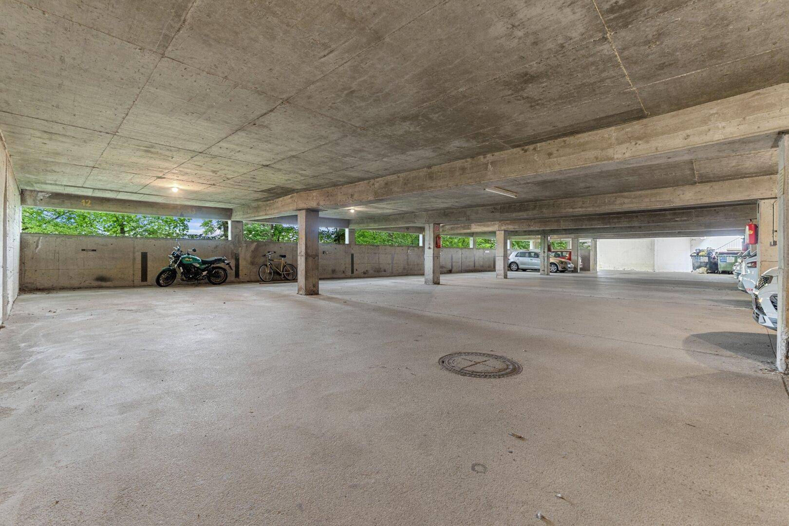 Große Tiefgarage mit Betonboden und ausreichend Stellplätzen für Fahrzeuge.