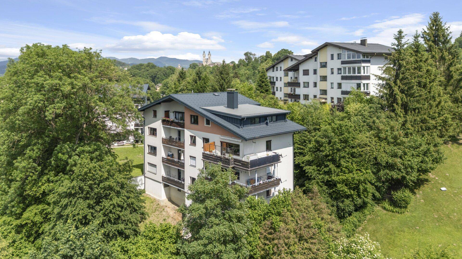 Luftaufnahme des modernen Mehrfamilienhauses, eingebettet in eine grüne Hügellandschaft.