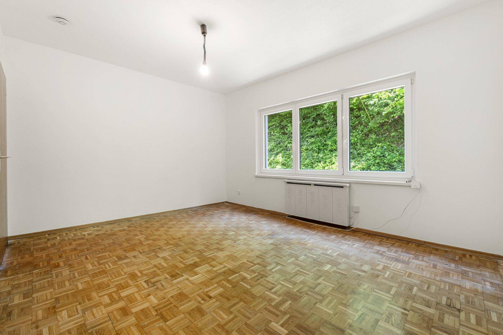 Helles Zimmer mit Parkettboden und großem Fenster, das viel Tageslicht hereinlässt.