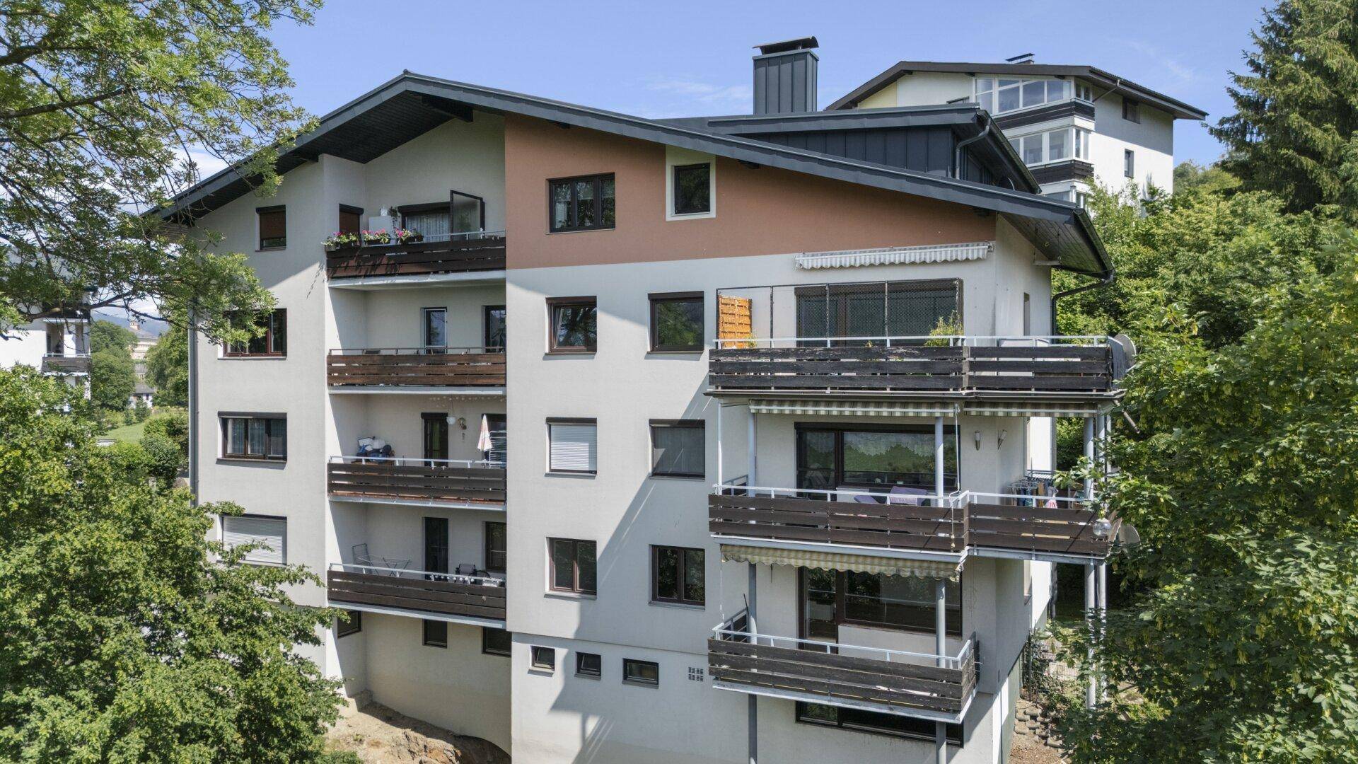 Ansicht des Gebäudes mit mehreren Balkonen und großen Fenstern, umgeben von Bäumen.