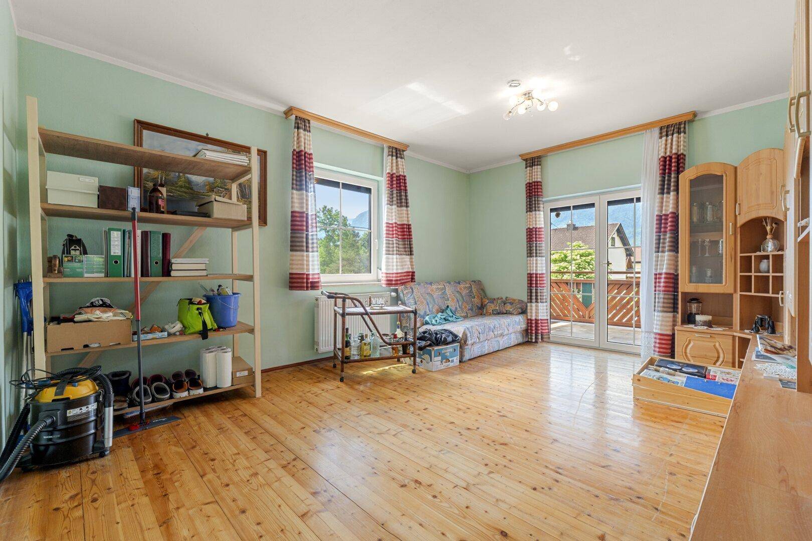 Helles Zimmer mit Holzboden, grünen Wänden und Zugang zu einem kleinen Balkon.