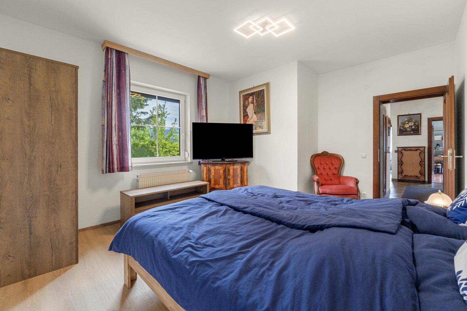 Schlafzimmer mit Holzboden, weiß gestrichenen Wänden und Blick ins Grüne.