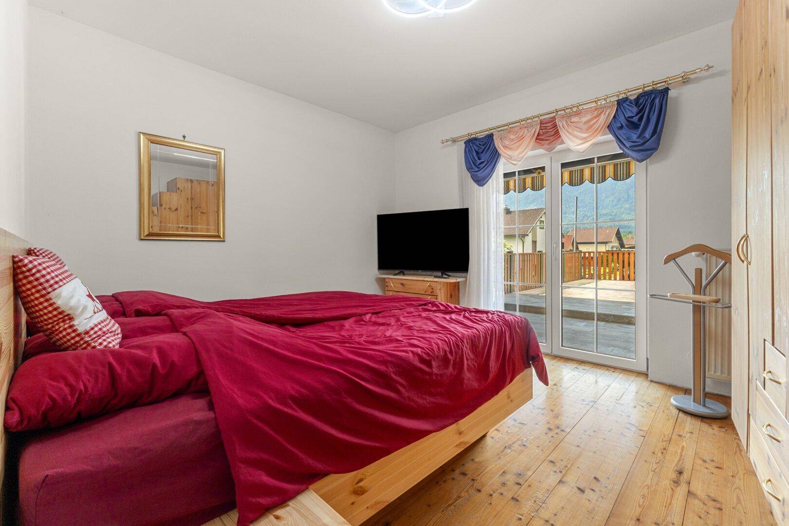 Schlafzimmer mit Holzboden, Zugang zum Balkon und traditioneller Dekoration.