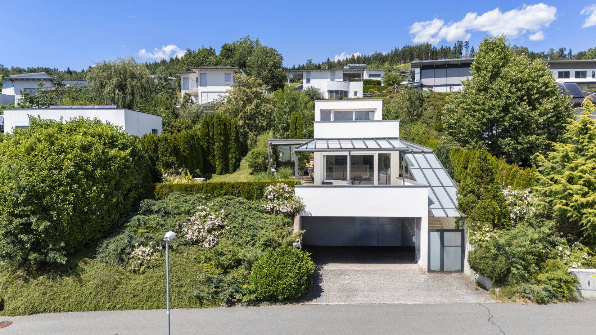 Modernes Wohnhaus in Hanglage mit integrierter Garage und umliegender grüner Landschaft.