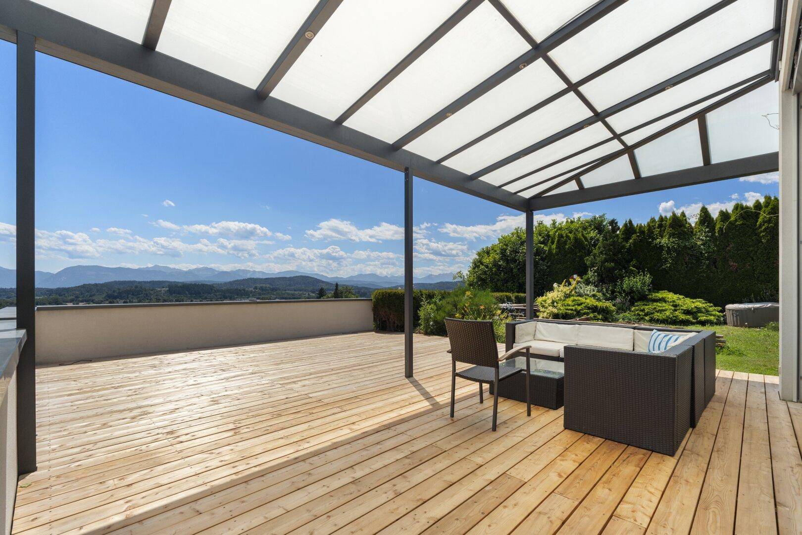 Geräumige überdachte Holzterrasse mit Sitzgelegenheiten und weitem Blick auf die Berge.