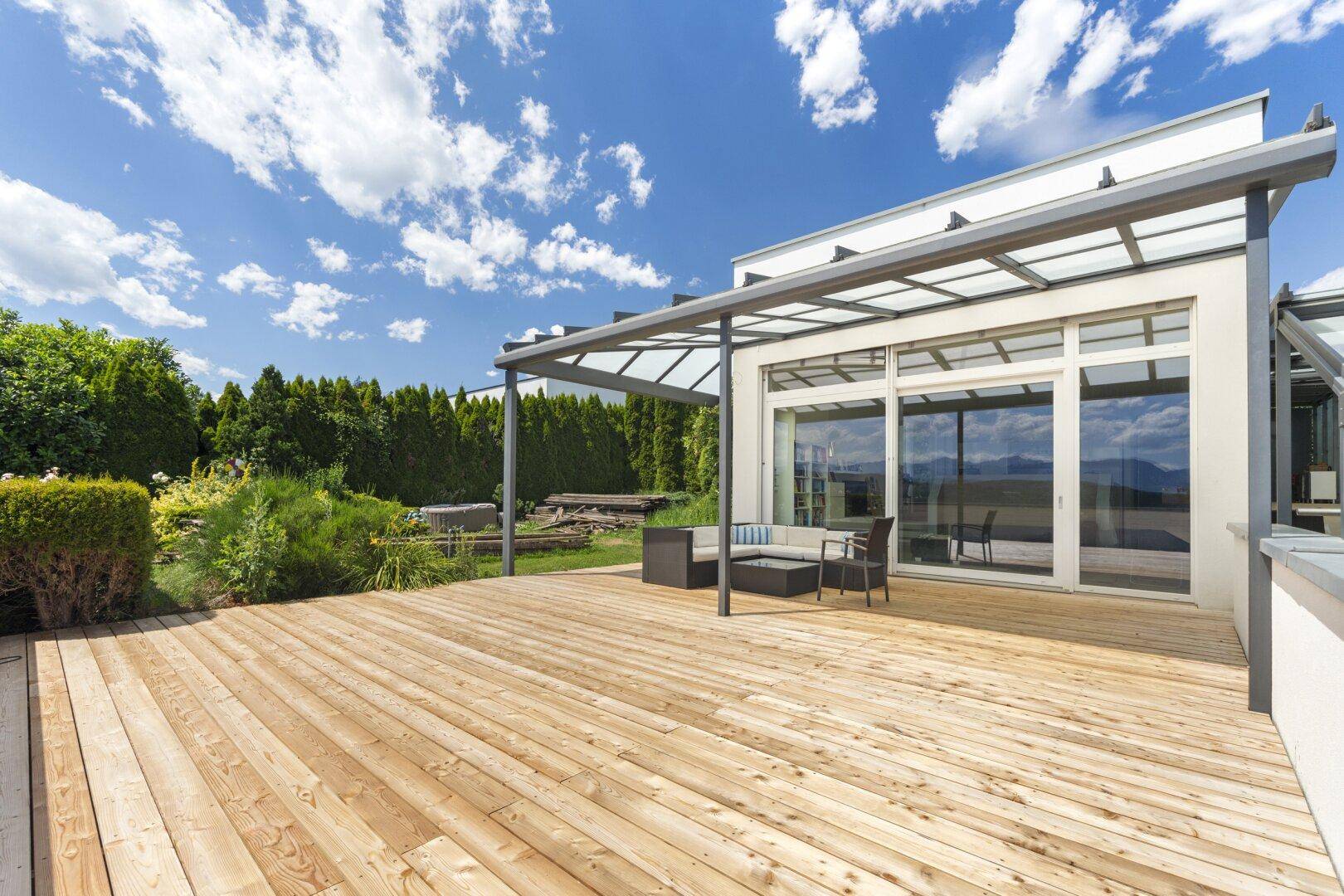 Große Holzterrasse vor dem modernen Haus mit weitem Blick und viel Sonnenlicht.