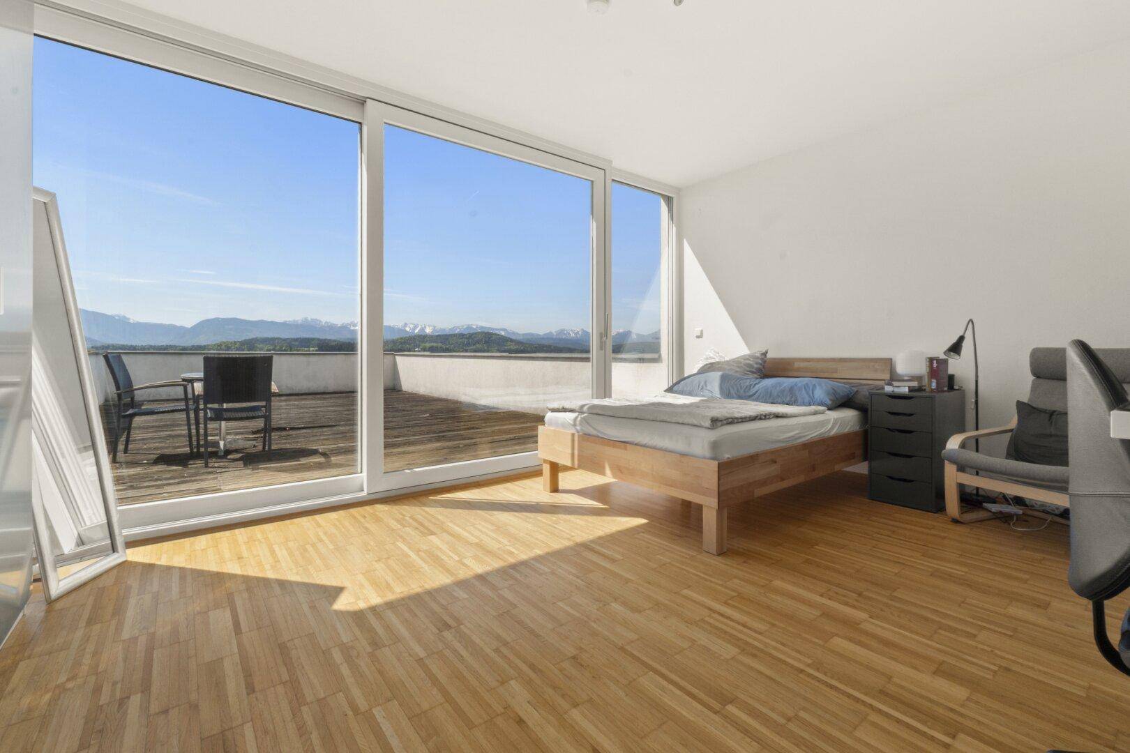 Helles Schlafzimmer mit Holzboden, großen Fenstern und direktem Zugang zur Terrasse mit Bergblick.