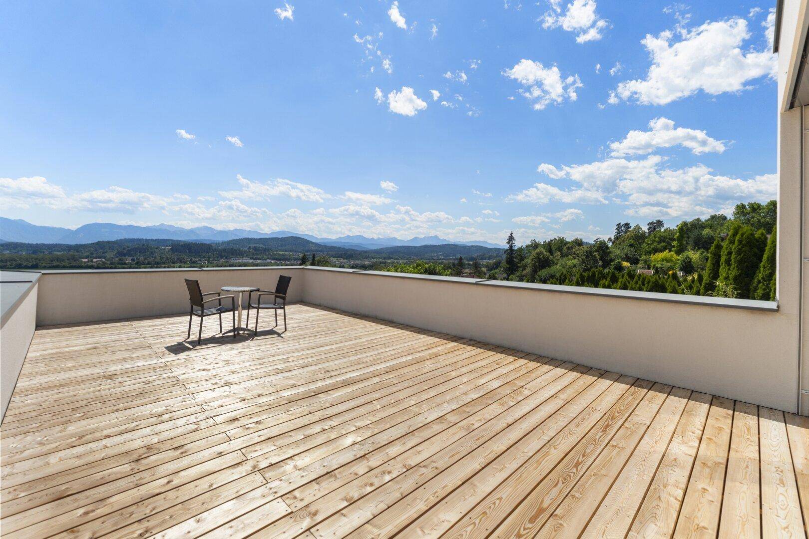 Offene Holzterrasse mit minimalistischen Möbeln und atemberaubendem Panoramablick auf die Berglandschaft.