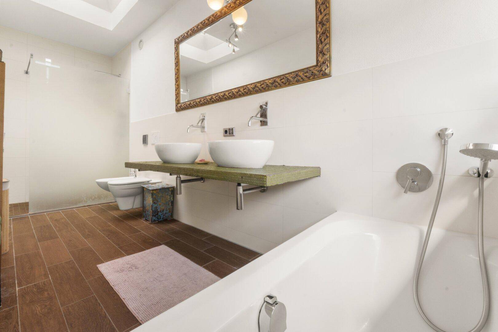 Modernes Badezimmer mit Doppelwaschbecken, Badewanne und Holzboden in warmen Farbtönen.
