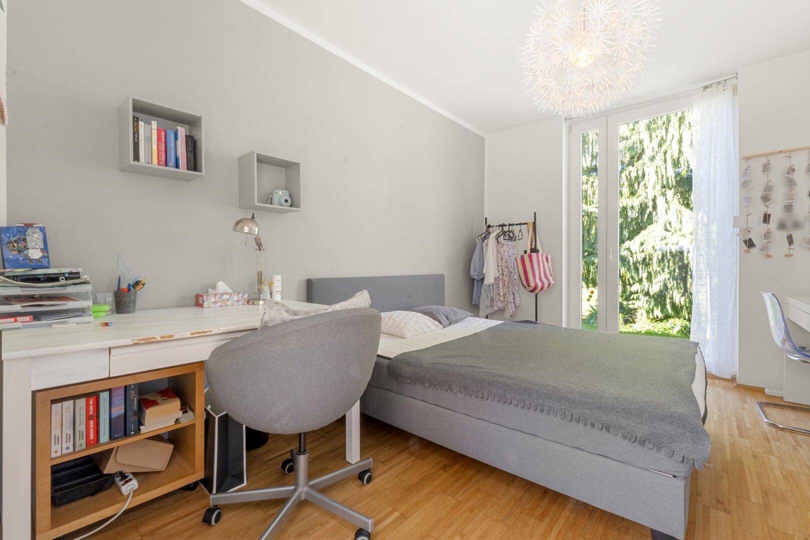 Helles Schlafzimmer mit Schreibtisch, Holzboden und Zugang zum Garten durch eine große Tür.