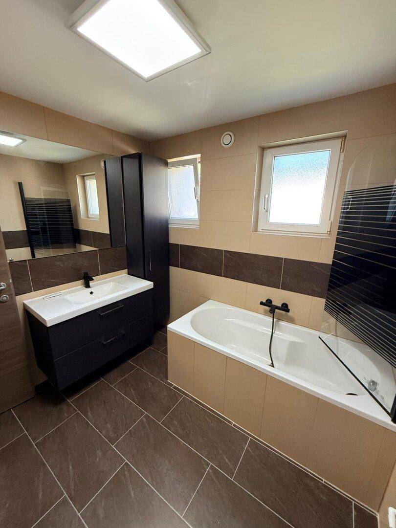 Modernes Badezimmer mit Badewanne, Einzelwaschbecken und beheiztem Handtuchhalter.