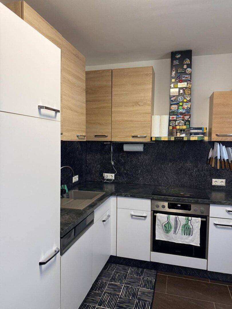 Moderne Küche mit weißen und holzfarbenen Schränken sowie dunkler Arbeitsplatte.