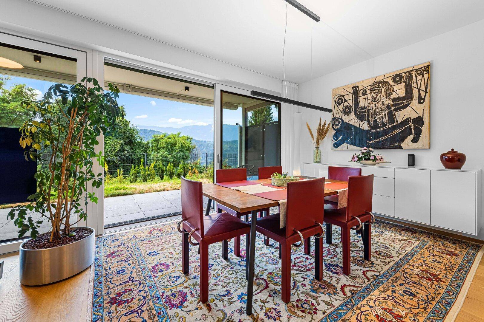 Essbereich mit großem Tisch und roten Stühlen, direktem Zugang zur Terrasse und Bergblick.