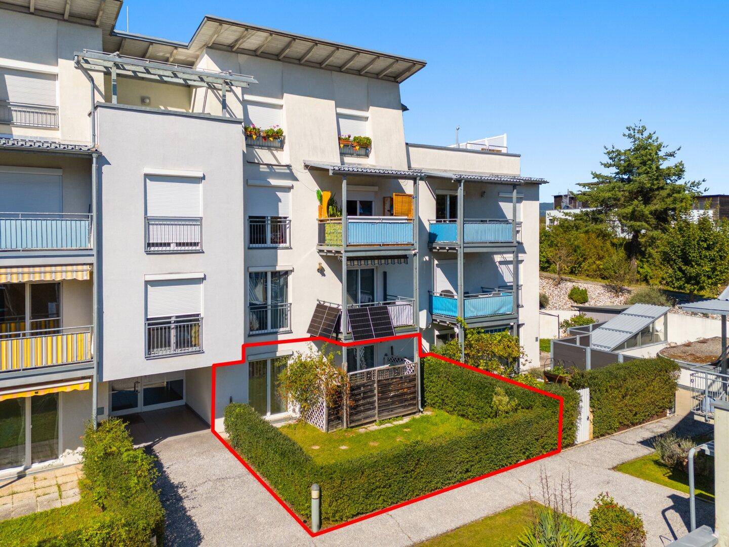 Ansicht der Gebäudefassade mit Balkonen, Rollläden und einem privaten Gartenbereich im Erdgeschoss.