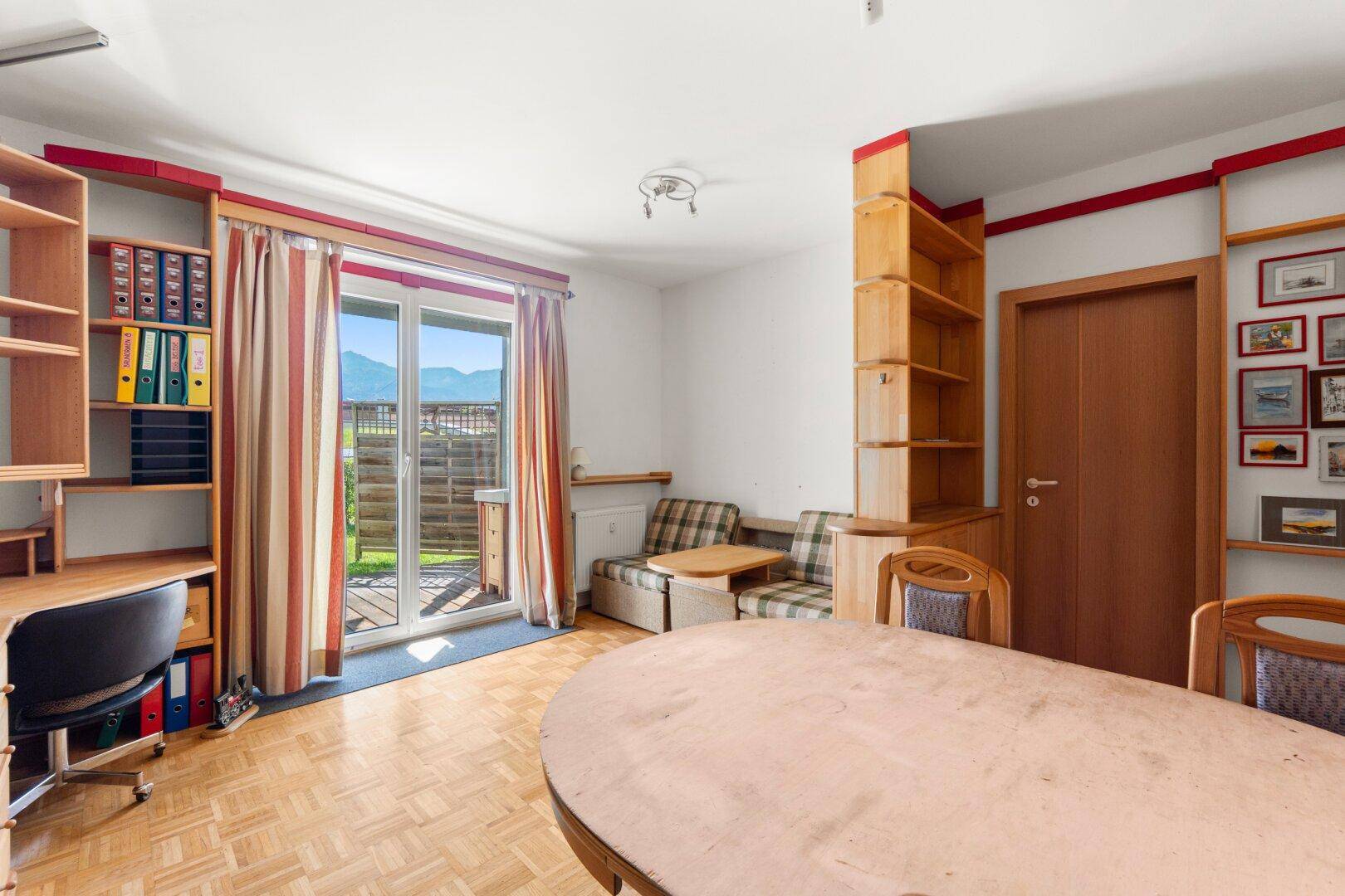 Heller Wohn- und Essbereich mit Parkettboden, Holzregalen und Zugang zu einem Balkon mit Bergblick.