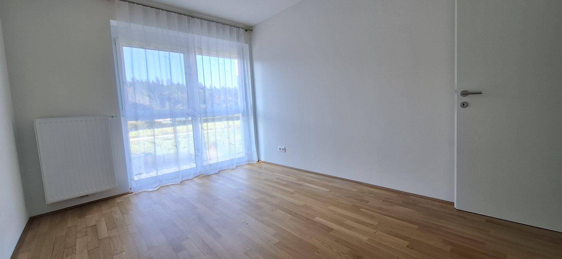 Helles Zimmer mit Holzboden und großem Fenster, das viel Tageslicht hereinlässt.