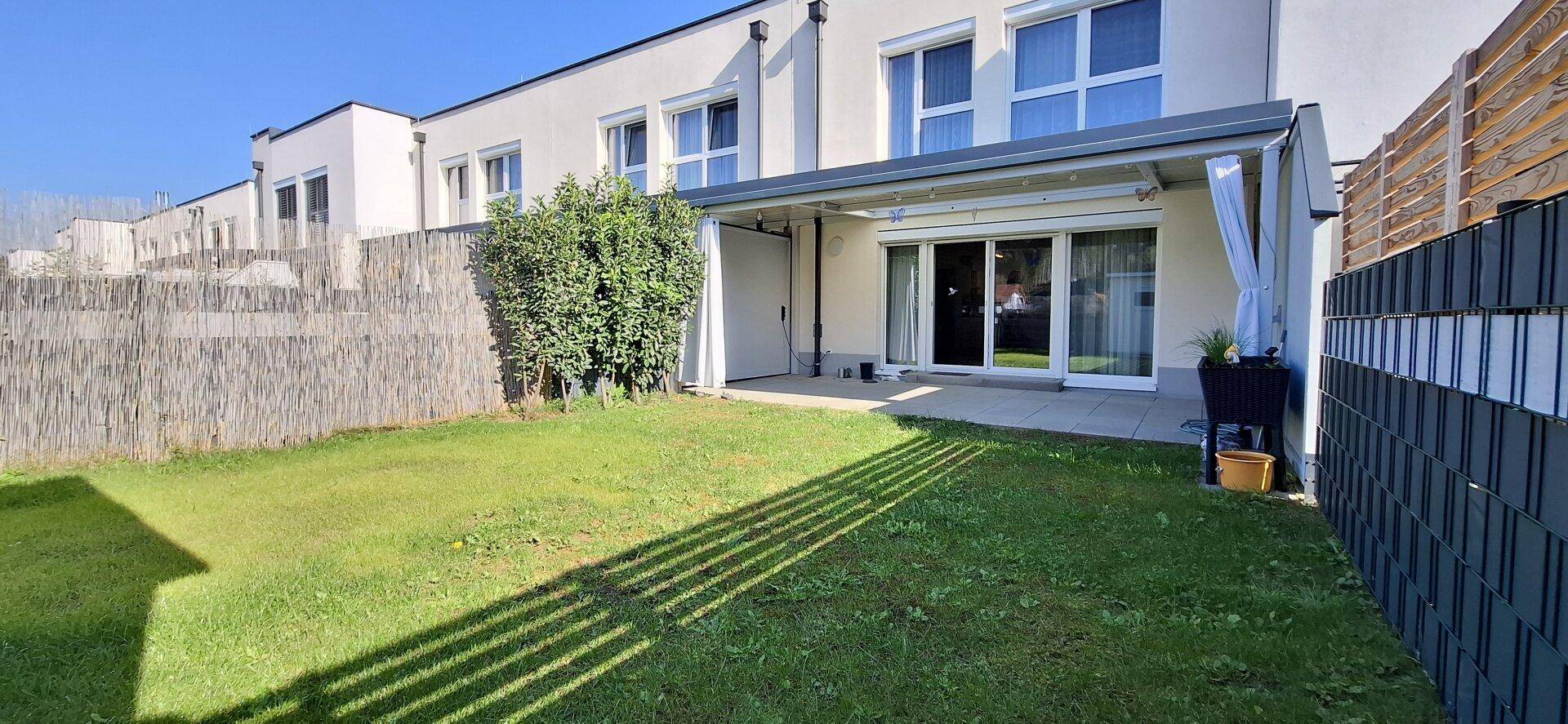 Gepflegter Gartenbereich mit Rasenfläche und überdachter Terrasse hinter einem Reihenhaus.