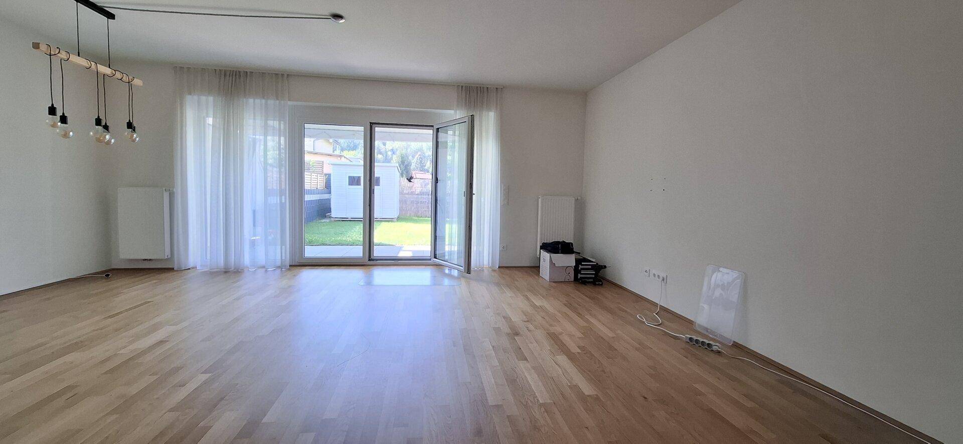 Geräumiges Wohnzimmer mit Holzboden und direktem Zugang zum Garten durch große Glastüren.