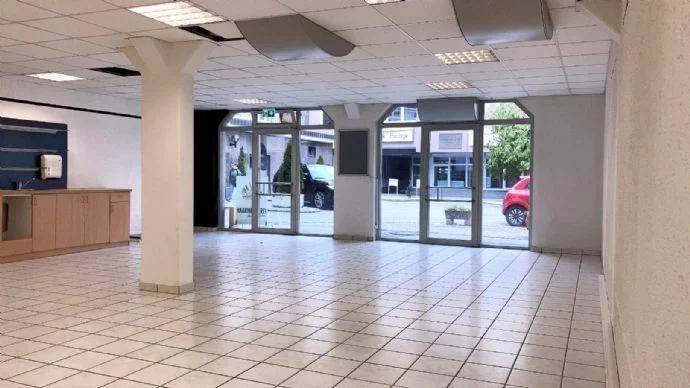 Geräumiger Ladenbereich mit hellen Fliesen, einer Säule und großen Fensterfronten zur Straße hin.