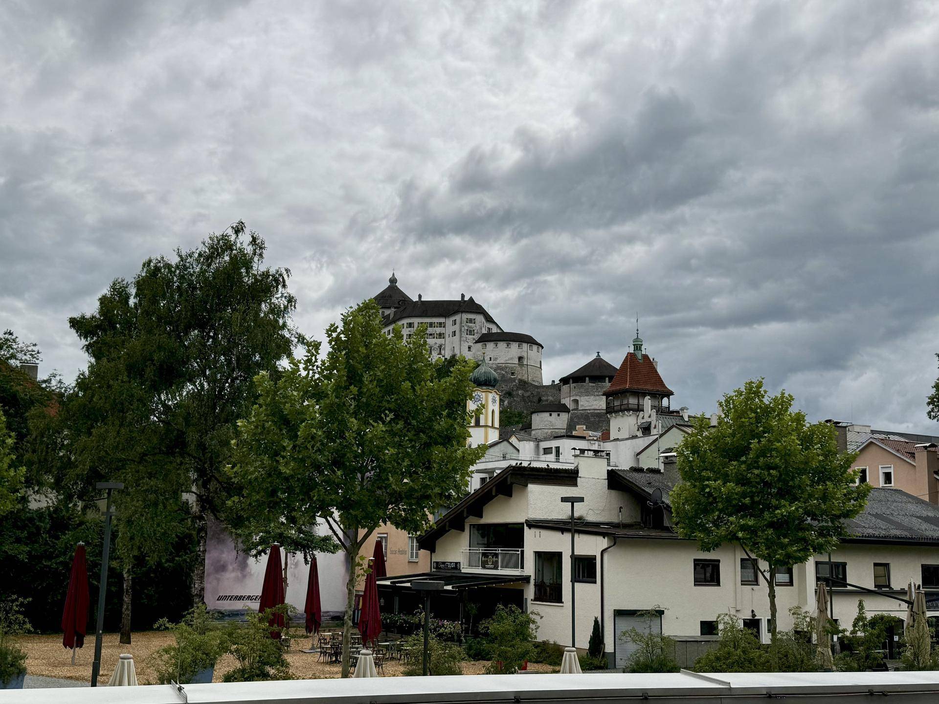 Panoramablick auf eine historische Stadt mit einer imposanten Burg auf einem Hügel unter bewölktem Himmel.
