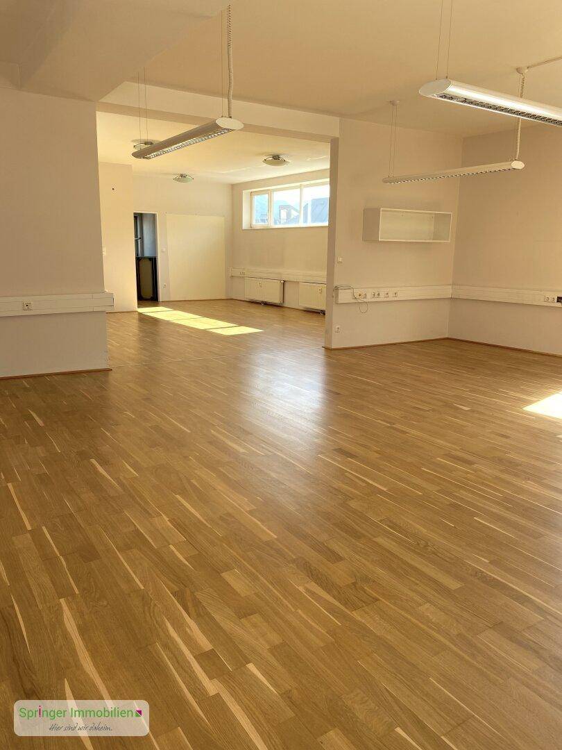 Geräumiger, heller Büroraum mit Holzparkettboden und großen Fenstern, ideal für gewerbliche Nutzung.