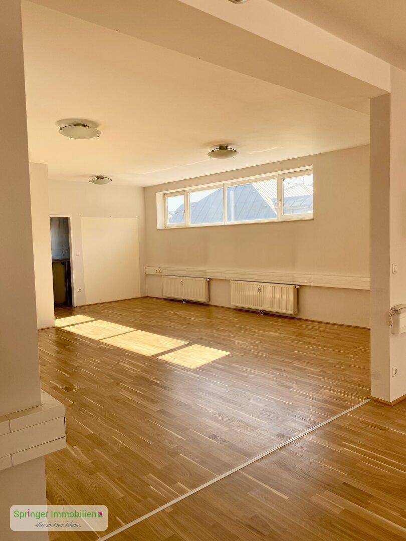 Heller Büroraum mit Holzboden und mehreren Fenstern, die viel Tageslicht hereinlassen.