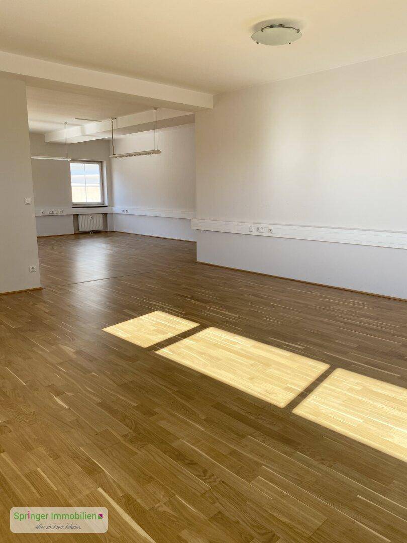 Weitläufiger Bürobereich mit hellem Holzfußboden und weißen Wänden, durchflutet von Sonnenlicht.