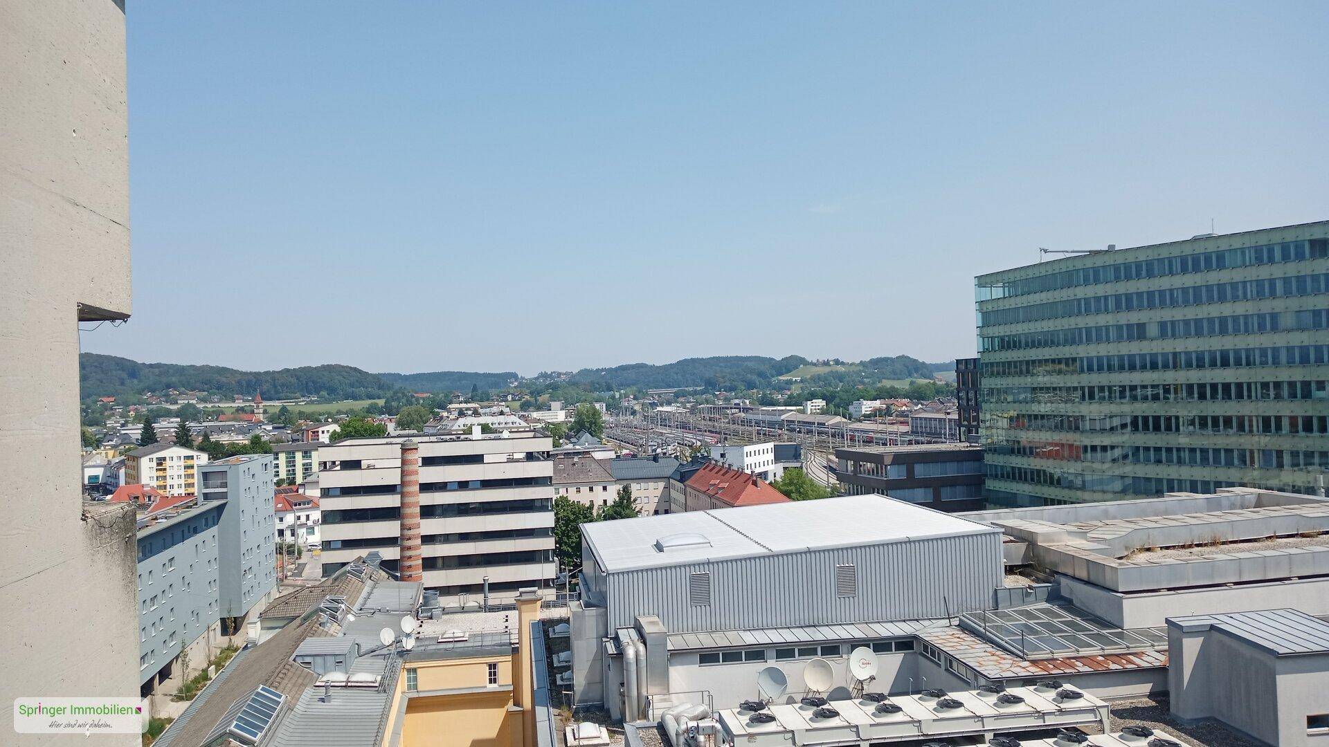 Panoramablick über die Stadt an einem sonnigen Tag, mit vielen Gebäuden und Grünflächen.