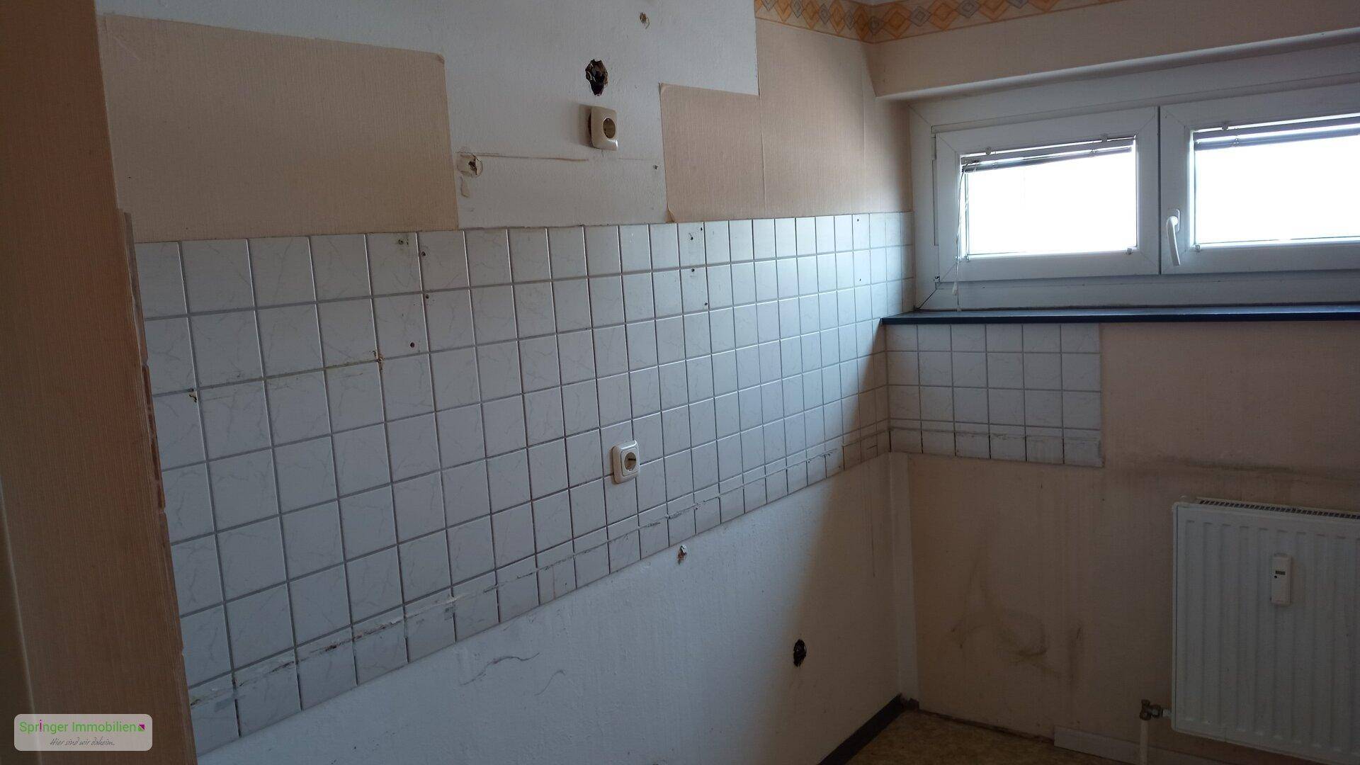 Unfertige Küche mit alten Fliesen an der Wand und einem Fenster, das auf Renovierung wartet.