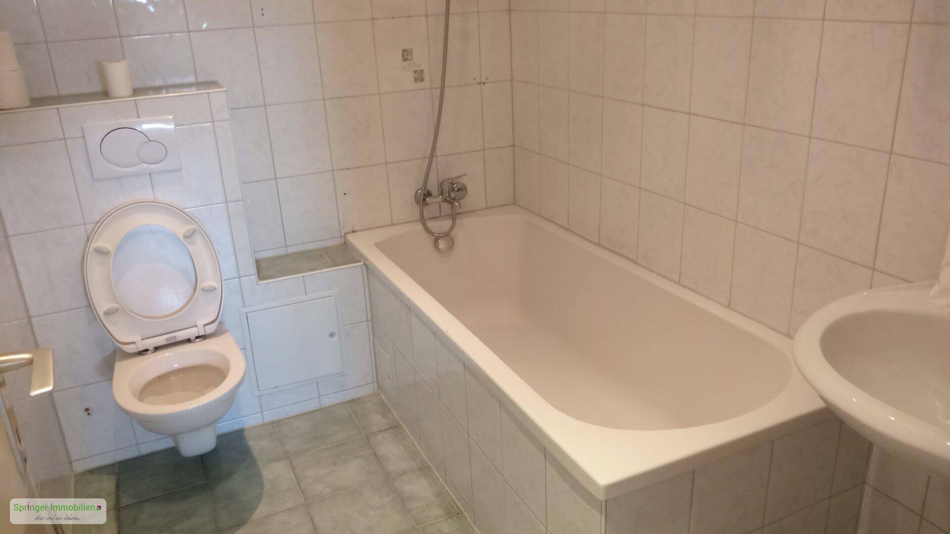 Badezimmer mit Badewanne, Toilette und Waschbecken, komplett gefliest in hellem Design.