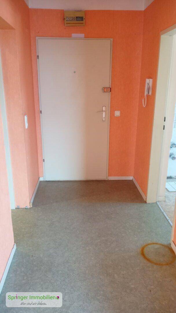 Eingangsbereich mit leuchtend orangefarbenen Wänden und einem robusten Bodenbelag.