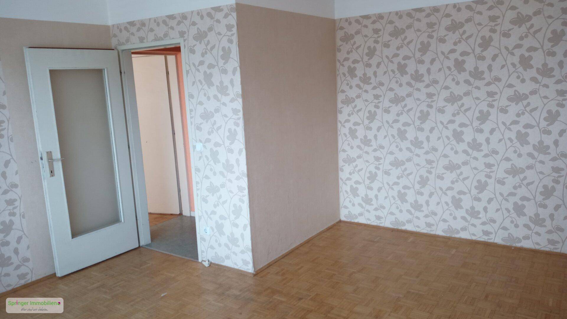 Leerer Raum mit gemusterter Tapete und Parkettboden, bereit für die individuelle Gestaltung.