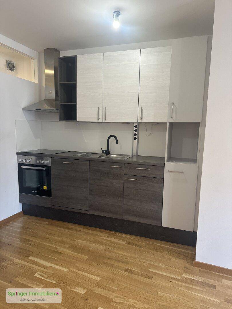 Moderne Küchenzeile mit grauen und weißen Schränken, integriertem Backofen und Dunstabzugshaube.