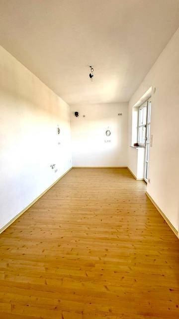 Heller Raum mit Holzoptik-Boden und einem Fenster, das viel Tageslicht hereinlässt.