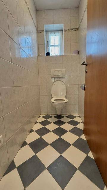 Separate Toilette mit Schachbrettmuster-Fliesenboden und wandmontiertem WC.